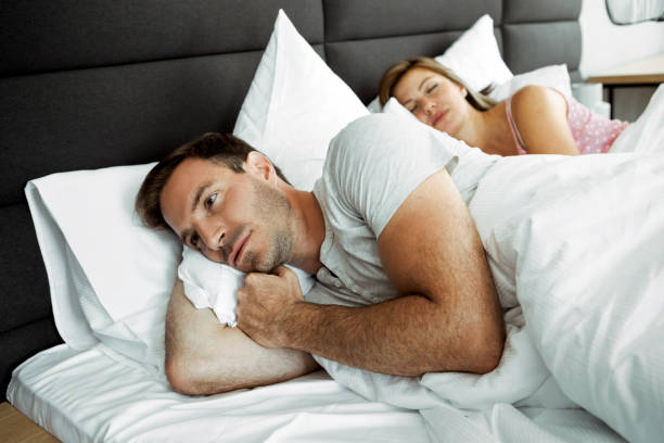 Man in bed can not sleep because his wife is snoring Woman in bed can not sleep because her husband is snoring worried man funny stock pictures, royalty-free photos & images