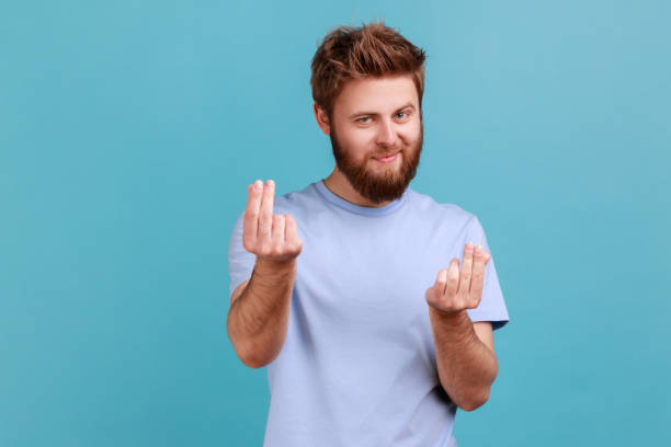Man in blue T-shirt rubbing fingers showing money gesture, asking for salary, demanding bribe. stock photo
