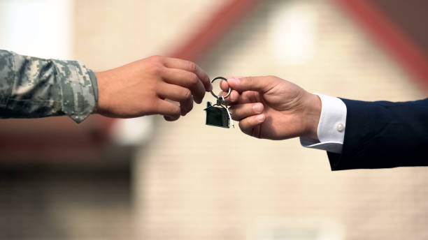 Man in business suit giving house key to man in military uniform, state support Man in business suit giving house key to man in military uniform, state support military lifestyle stock pictures, royalty-free photos & images