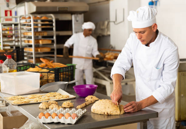 man in chefs uniform kneading dough in bakery stock photo