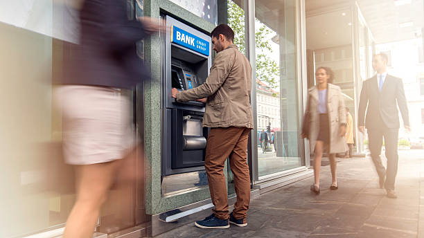 Man in front of an ATM machine Focus on man standing in front of an ATM machine on a city street, defocused incidental people. bank financial building stock pictures, royalty-free photos & images