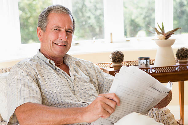 Man sitting in living room reading newspaper smiling