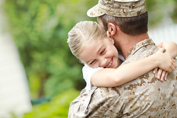 Man in military uniform carrying a little girl A father who is back from the army hugging his daughter who is smiling and embracing her father soldiers returning home stock pictures, royalty-free photos & images