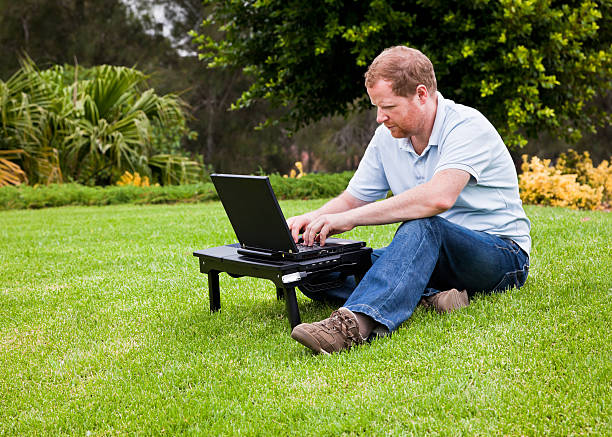 Man in park using wireless laptop computer stock photo