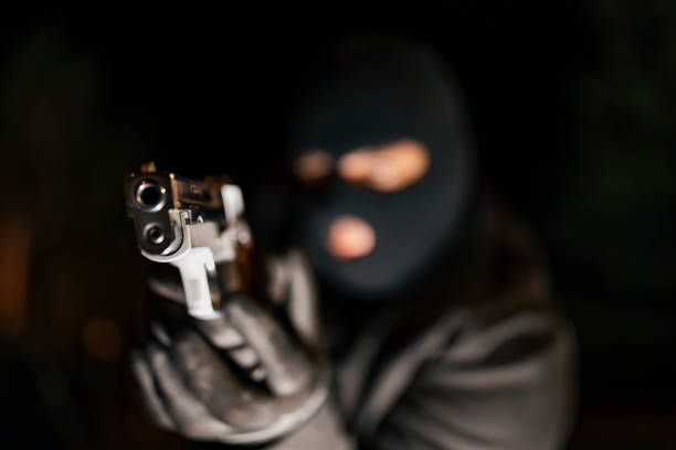 Man in skin mask holding gun A man holding a gun in hand, the ship ready to shoot the man pointed a gun at us. A man holding a gun was robbed. ski mask criminal stock pictures, royalty-free photos & images