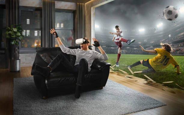 Man in VR Glasses. Virtual Reality with children's soccer Young man at home on a black sofa with VR headset emotionally playing in virtual reality children's soccer virtual reality point of view stock pictures, royalty-free photos & images