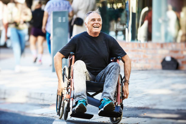 Man in wheelchair smiles and laughs as he powers across a city intersection, crossing the street stock photo