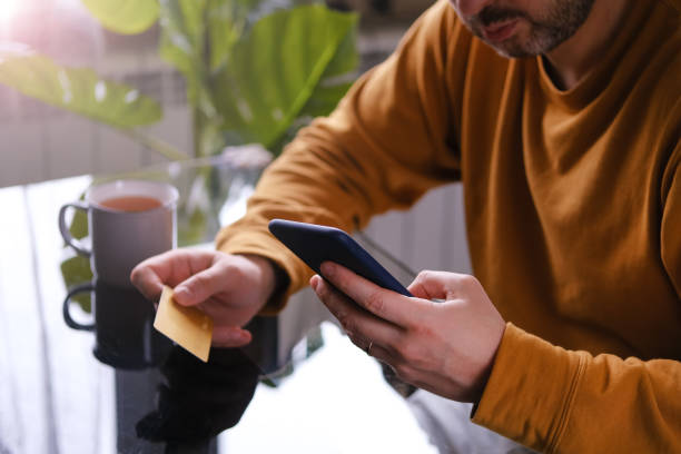 Man in yellow pajamas sitting at the table with credit card and phone shopping online stock photo