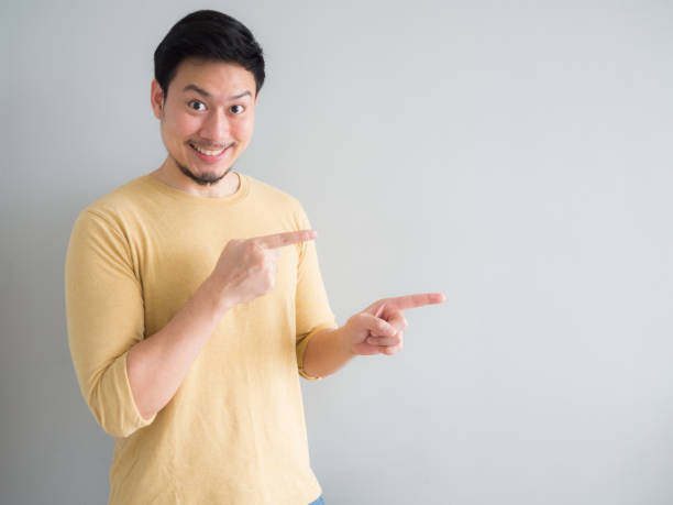 Man in yellow t-shirt excited to point and present an empty space background. stock photo