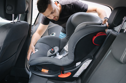 Man installs a child car seat in car at the back seat. Responsible father thought about the safety of his child.