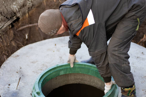 A man installs a sewer manhole on a septic tank made of concrete rings. Construction of sewer networks in the village stock photo