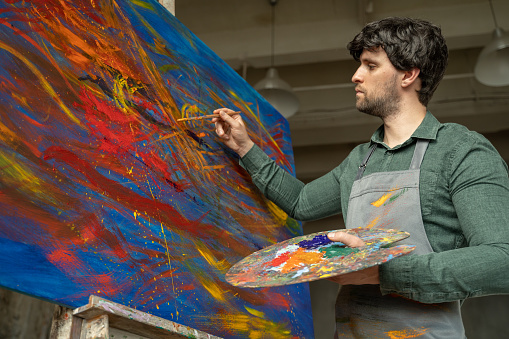 Man is an artist, holding a brush and drawing an abstract picture.