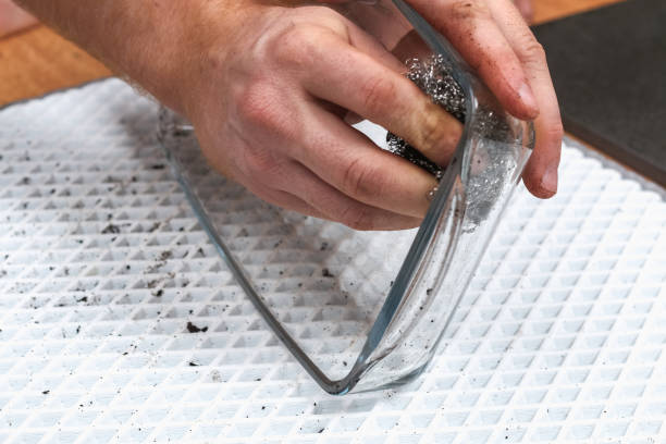 A man is cleaning dirty baking dish with a thick layer of carbon with an iron washcloth. Glassware for baking with soot, carbon deposits, old dried fat. stock photo