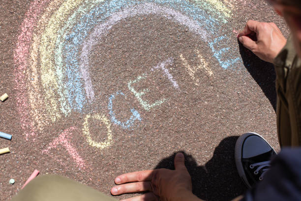 Man is drawing rainbow, symbol of lgbt Young man is sitting on a pavement and drawing rainbow during pride month. Freedom, diversity, acceptance, lgbt concept chalk drawing photos stock pictures, royalty-free photos & images
