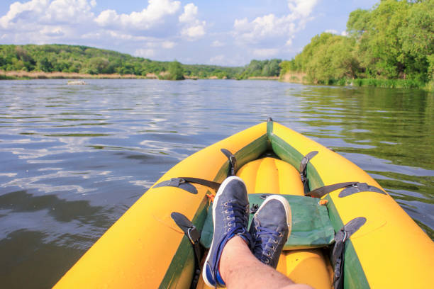Man is relaxation on yellow boat  the river. Close-up sneakers on the feet. View to the crossed feet on the boat. POV stock photo