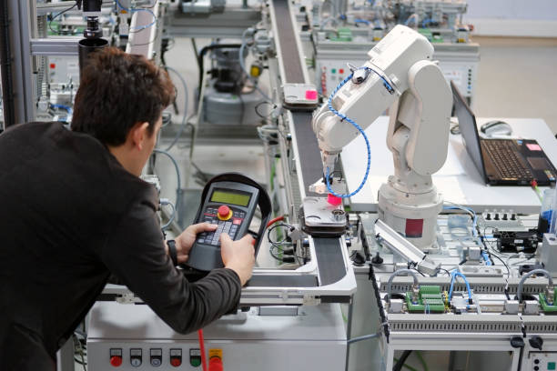 Man is working to control a robotic arm Man is working to control a robotic arm which is integrated on smart factory production line. industry 4.0 automation line which is equipped with sensors and robotic arm. Selective Focus. mechatronics stock pictures, royalty-free photos & images
