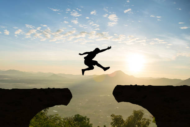 Man jump Mountain cliff sun light over silhouette stock photo