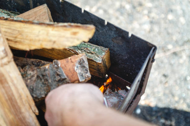 a man kindles a fire in a brazier with matches - idosos aquecedor imagens e fotografias de stock