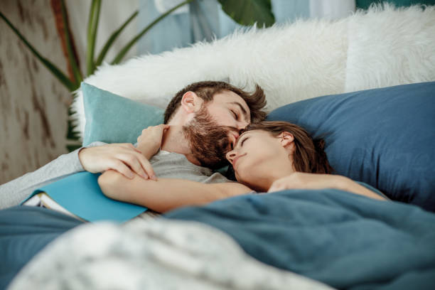 hombre besando a su novia mientras está acostado en la cama - durmientes en pareja  fotografías e imágenes de stock