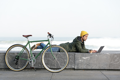 Hispanic digital nomad working on his laptop while laying beside bicycle