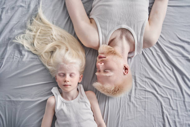 Man laying with his cute blonde daughter together at the bed with closed eyes stock photo