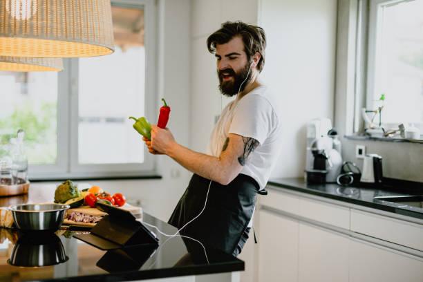 man listening to music and singing while cooking healthy food - plant based food imagens e fotografias de stock