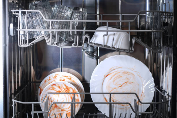 A man loads dirty dishes, plates, spoons, forks, cutlery into dishwasher tray. stock photo