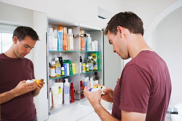 man looking at bottles from medicine cabinet - pijnstiller stockfoto's en -beelden