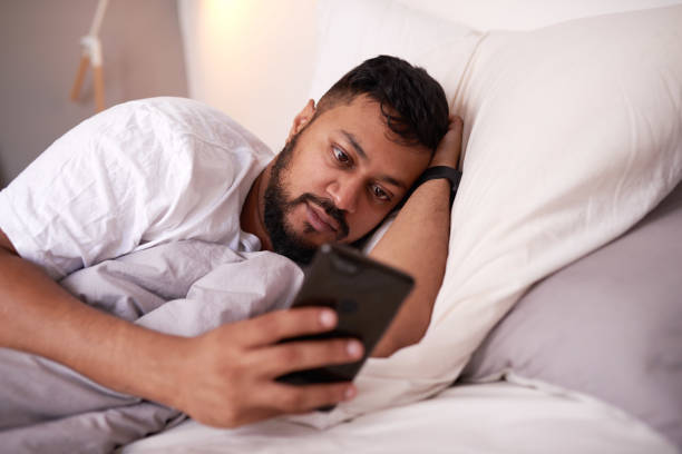 A man looking at his mobile phone while lying in bed stock photo
