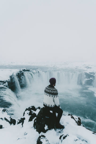 Man looking at scenic view of waterfall in winter Young Caucasian man in Icelandic sweater  looking at scenic view of waterfall in winter dettifoss waterfall stock pictures, royalty-free photos & images