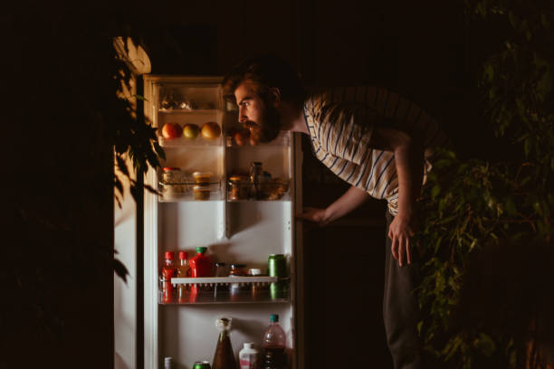 man looking for snacks in the refrigerator late night - come e sente imagens e fotografias de stock