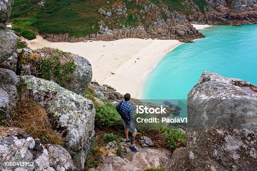 istock Man looking  over Porthcurno Beach, Pedn Vounder beach and Logan Rock  seen from Minack Open Air Theatre; Cornwall; England; UK 1050413952