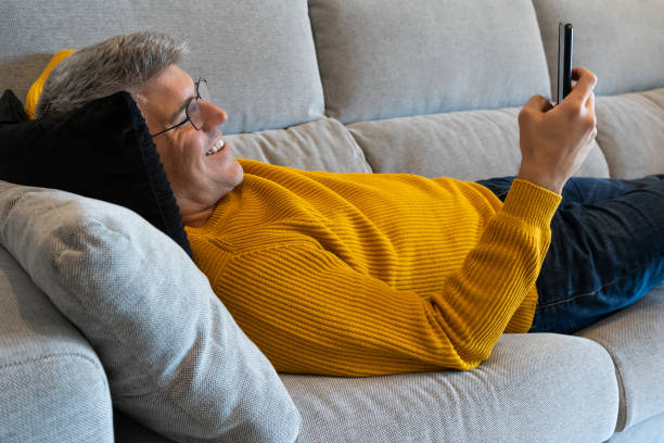 Man lying on the sofa looking his mobile phone. Concept relax at home stock photo