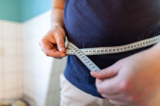 man measures her abdomen with a measuring tape stock photo