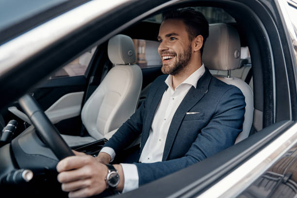 Man of style and status. Handsome young man in full suit smiling while driving a car man driving suit stock pictures, royalty-free photos & images