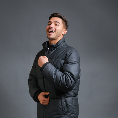 Smiling stylish guy model on a gray background is warmly dressed in a black down jacket. High quality photo