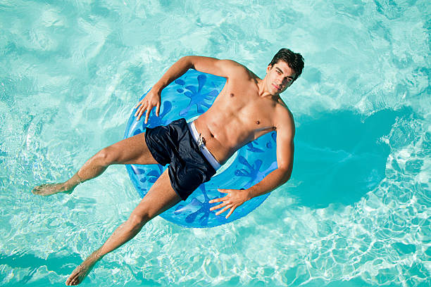 mann auf schwimmring im pool - badebekleidung stock-fotos und bilder