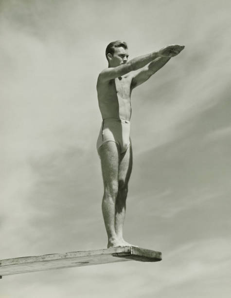 Man on springboard ready to jump, (B&W), low angle view  20th century stock pictures, royalty-free photos & images