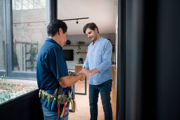 Man opening the door of his house to an electrician and signing a report stock photo