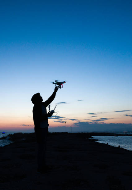 man werking van vliegende drone quadrocopter bij zonsondergang - man,standing, elevated view,remote control stockfoto's en -beelden