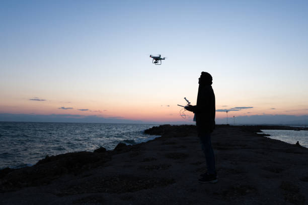 man werking van vliegende drone quadrocopter bij zonsondergang - man,standing, elevated view,remote control stockfoto's en -beelden