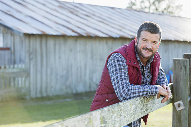 homme à l’extérieur de la grange adossé à une clôture en bois - portrait agriculteur photos et images de collection