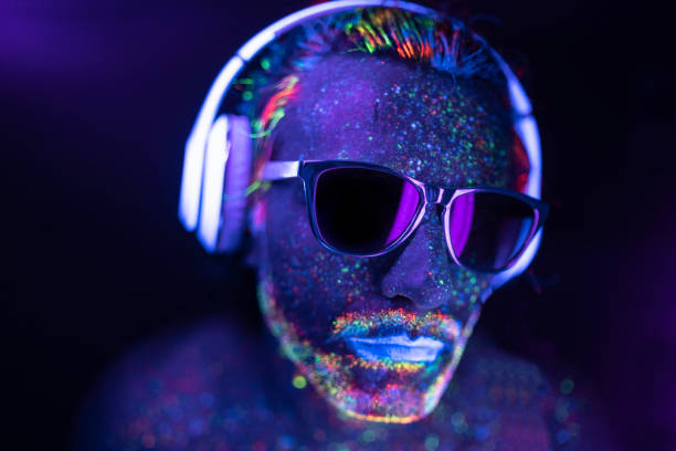 Man painted in neon colors with sunglasses and headset Man with glowing makeup in black light. Man with neon makeup powder on face. Man painted in fluorescent UV colors, with sunglasses and headset. paint neon color neon light ultraviolet light stock pictures, royalty-free photos & images