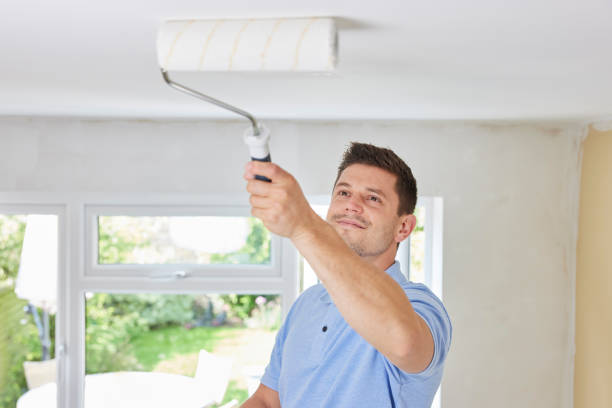 Man Painting Ceiling In Room Of House With Paint Roller stock photo