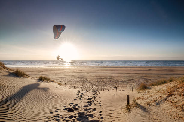 mens die op strand bij zonsondergang in de zomer parasiteert - nederland strand stockfoto's en -beelden