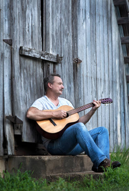 Man playing acoustic guitar leaning against barn stock photo