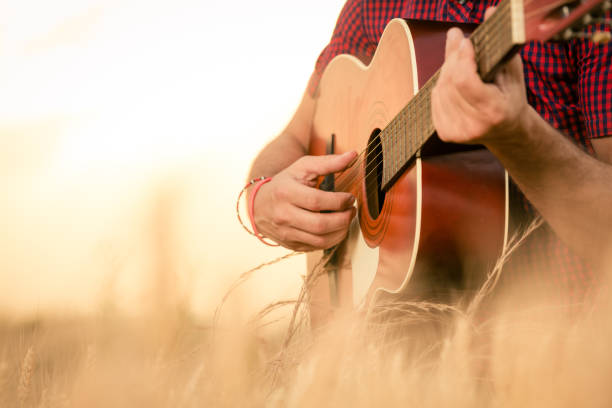 Man playing acoustic guitar on the field Close up of male hands playing acoustic guitar on the wheat field at the sunset. Retro, music, lifestyle concepts. country and western music stock pictures, royalty-free photos & images