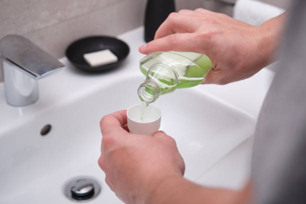 Man pouring green mouthwash from bottle into cap in bathroom. Teeth care concept. stock photo