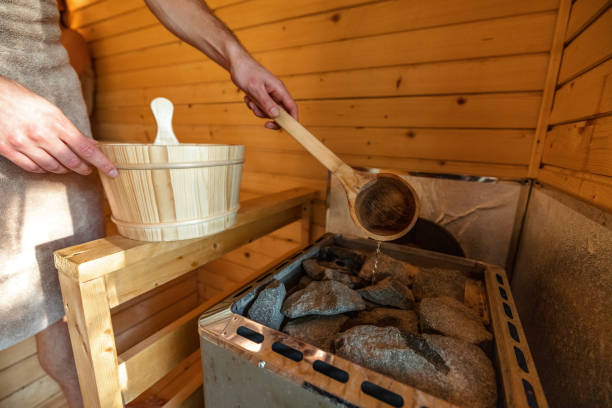 A Man Pouring Water On Hot Stones In Finnish Sauna stock photo