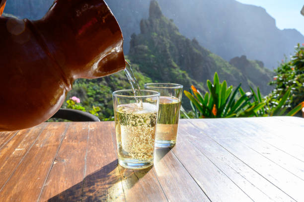 man pouring white wine from clay jug into glass on terrace with view on green landscapes of small mountain village masca on tenerife, spain - cargo canarias imagens e fotografias de stock